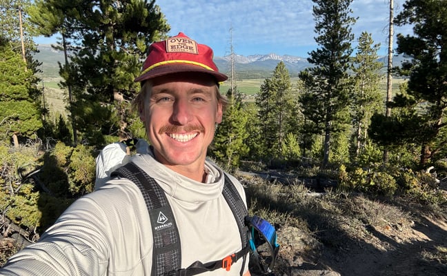 Rock climber hanging upside down from rope with forested river valley below